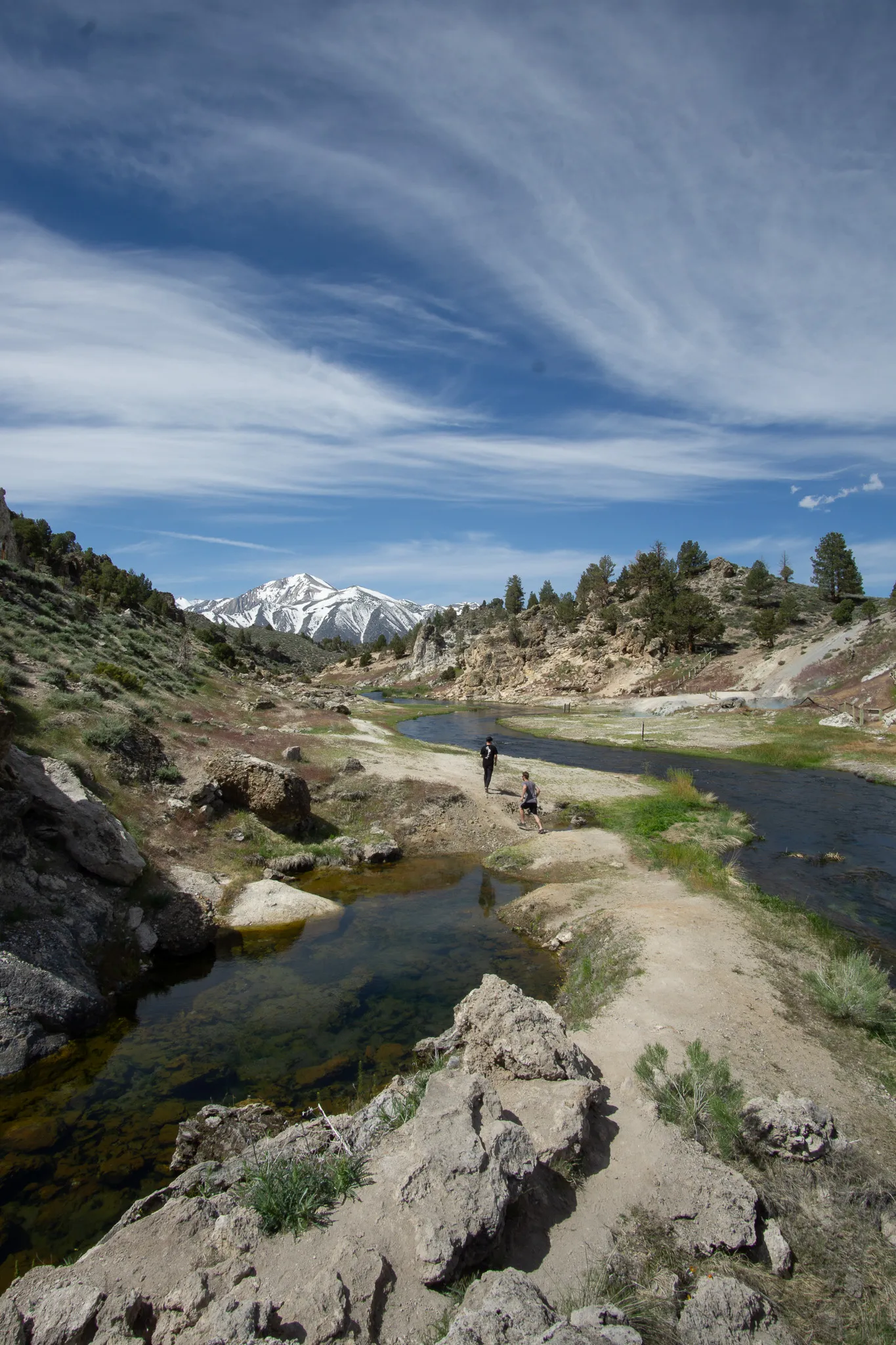 Winding creek through a rocky alpine valley with snowy mountains and cirrus clouds overhead