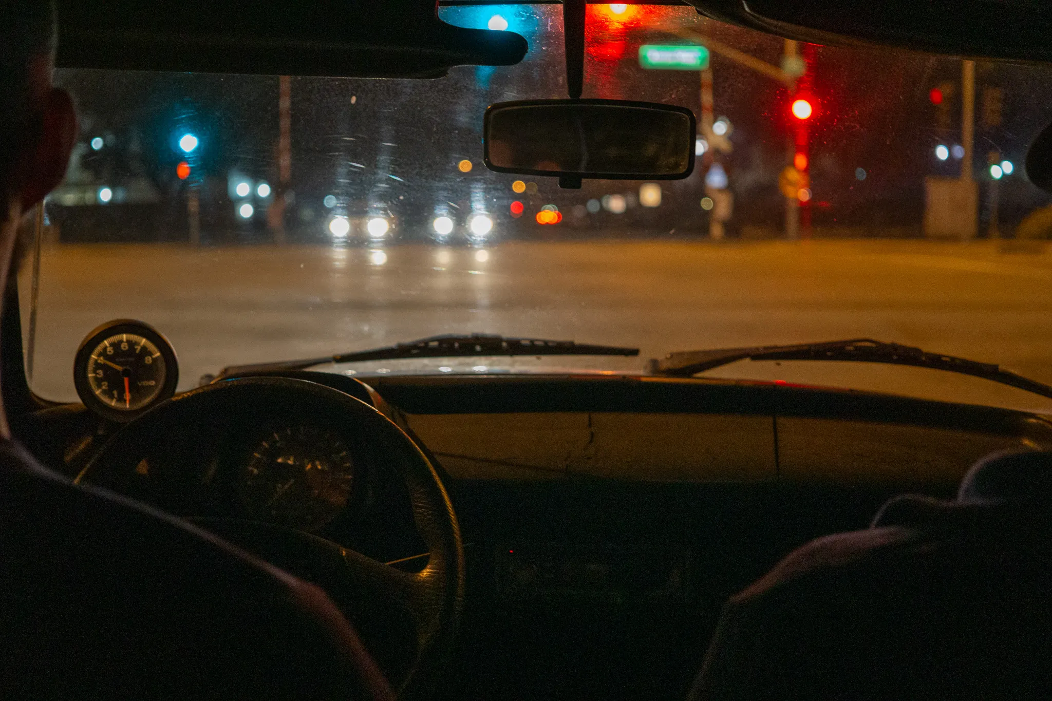 Dashboard and steering wheel of a vintage VW Bug facing nighttime traffic lights and headlights